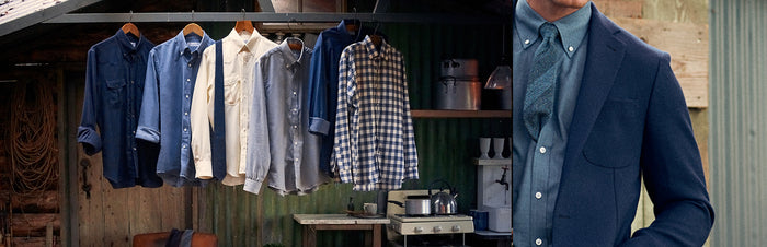A row of collared shirts in various colors hangs on a rack beside rustic kitchenware, with a man in a blue suit and patterned tie standing partially in view on the right.