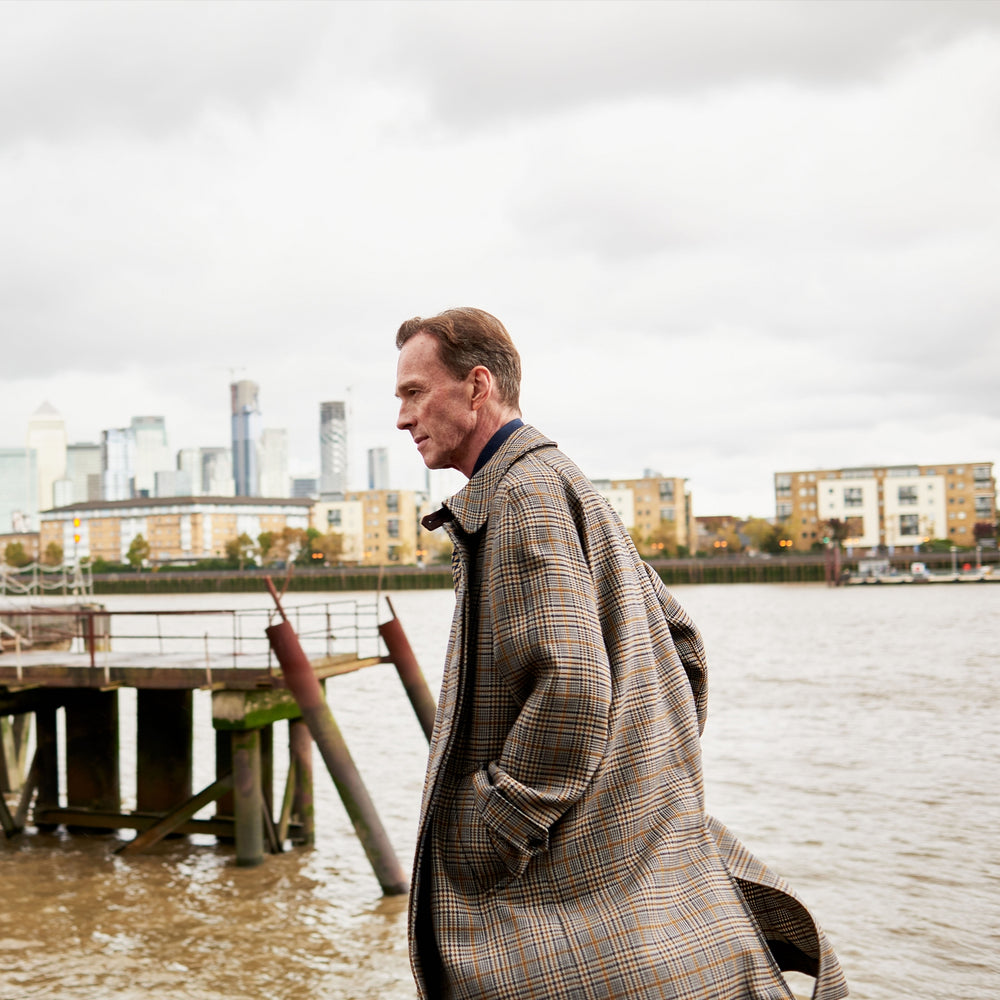 The Turnbull & Asser Checked Wool Car Coat features a straight-cut silhouette in brown and gray Prince of Wales check, classic collar, concealed front buttons, long sleeves, and a minimalist tailored design.