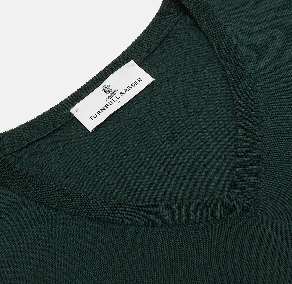 The Turnbull & Asser Forest Green Fine Merino V-Neck Jumper, shown laid flat on a white background, features classic Scottish knitwear details with ribbed cuffs and hem for a timeless look.