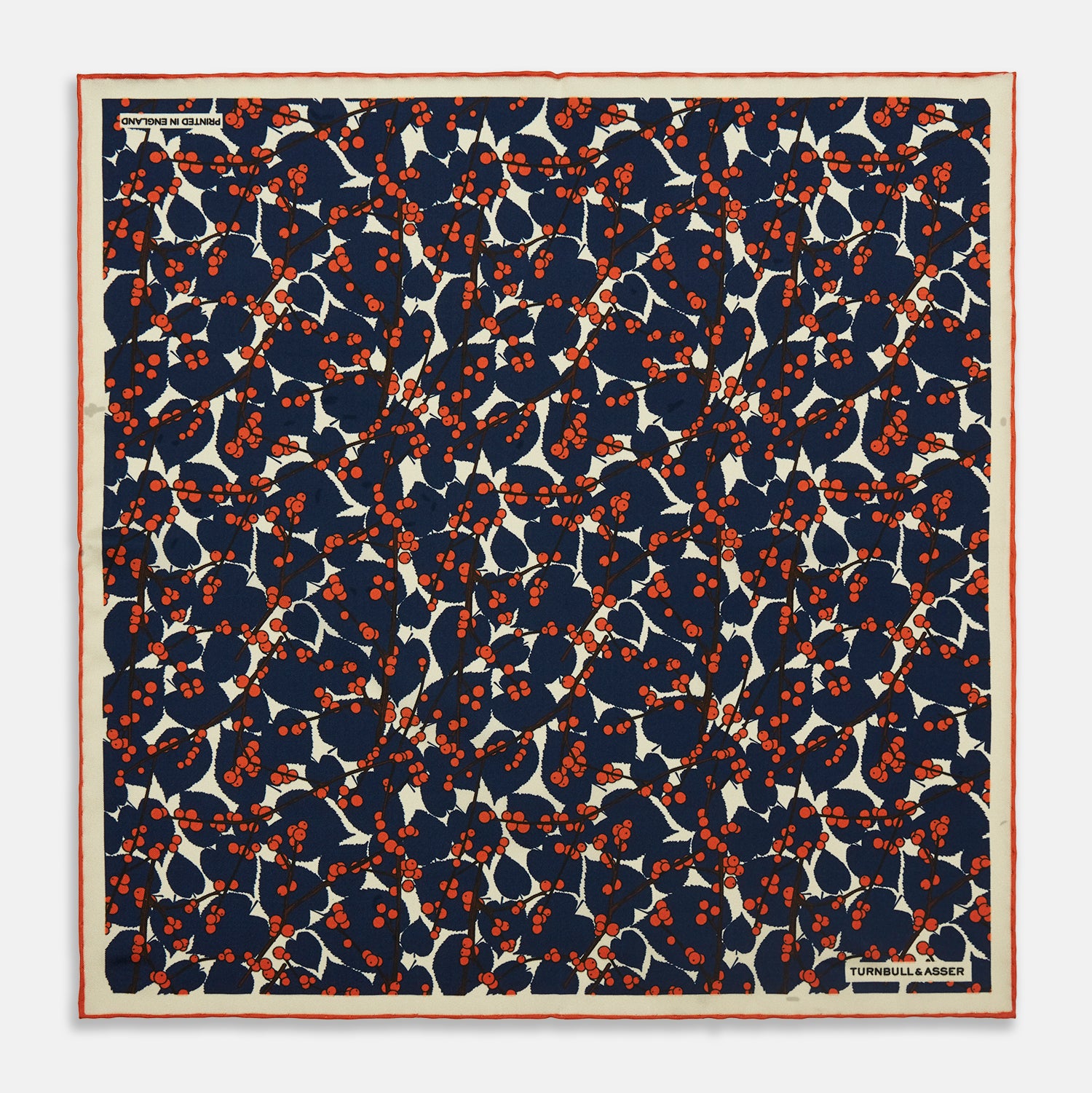 View 1 of product The Blue Berry Floral Pocket Square by Turnbull & Asser features a navy blue silk background with red berry and white leaf designs, plus small labels on two corners—making it a perfect festive gift.