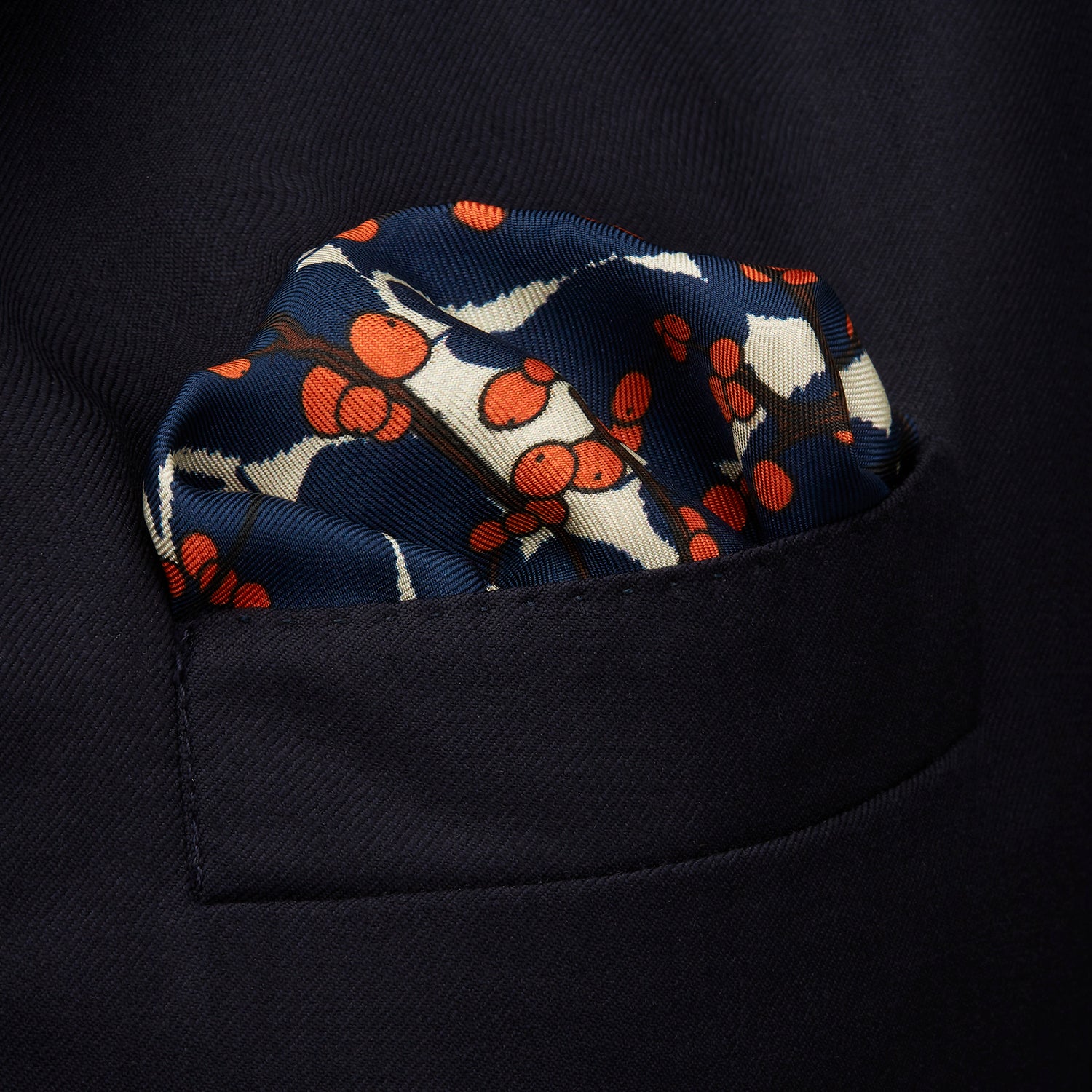 View 3 of product The Blue Berry Floral Pocket Square by Turnbull & Asser features a navy blue silk background with red berry and white leaf designs, plus small labels on two corners—making it a perfect festive gift.