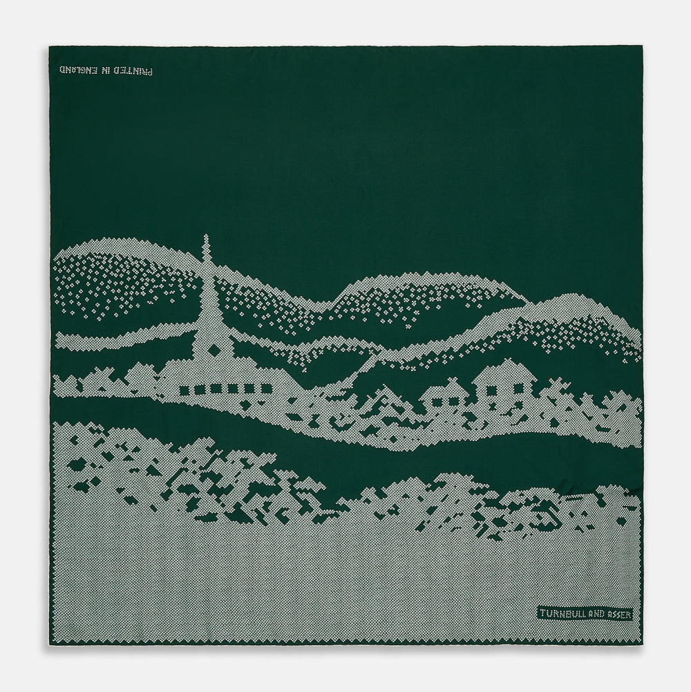 The Green Snowscape Motif Silk Extra Large Scarf by Turnbull & Asser features a white embroidered winter landscape with hills, trees, a church, and houses. "TURNBULL AND ASSER" appears in the corner. Made in England—perfect for winter.