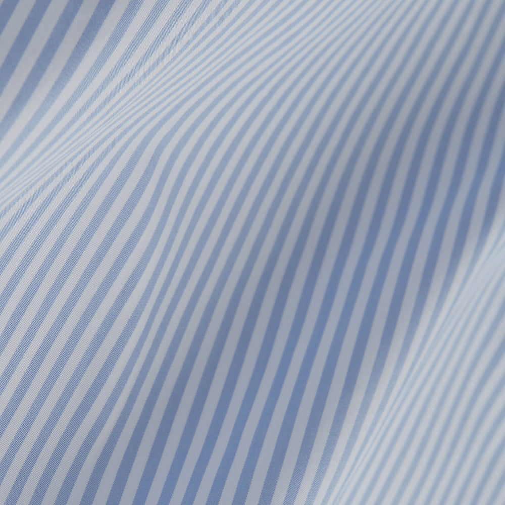 The Turnbull & Asser Light Blue Bengal Stripe Shirt features white vertical stripes, a classic T&A collar, and 3-button cuffs. Buttoned down the front, it’s laid flat on a white background for a timeless British look.