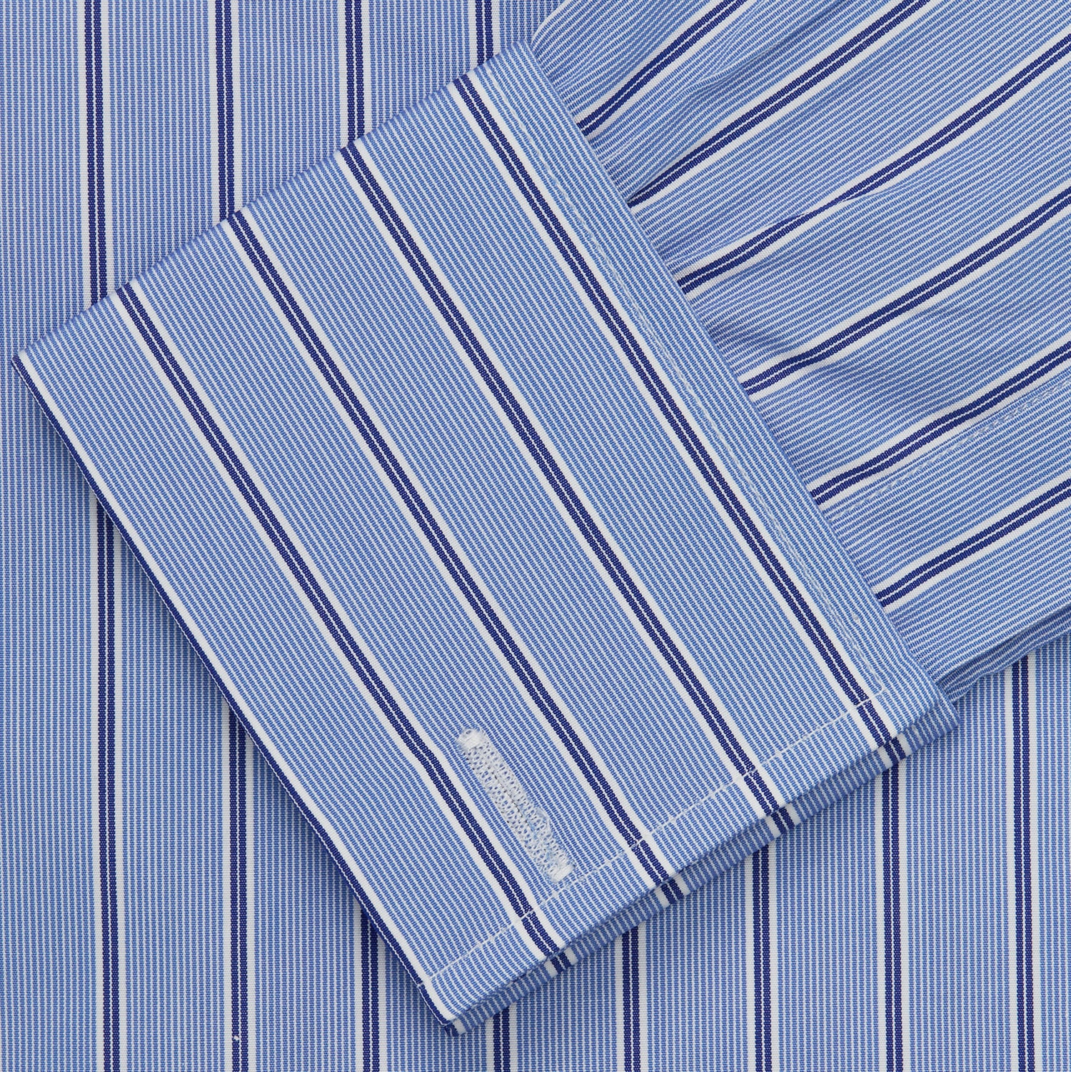 View 5 of product A neatly folded Turnbull & Asser Blue Stripe Regular Fit Shirt with T&A collar and square double cuffs, featuring long sleeves and thin white stripes on a light blue base, displayed on a plain white background.