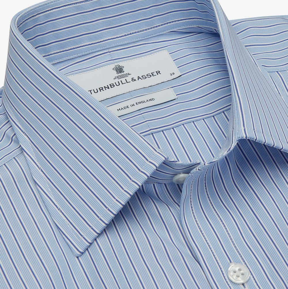 Turnbull & Asser’s Blue Stripe Shirt features thin vertical white stripes, a T&A collar, 3-button cuffs, white buttons, and a regular fit. Smart-casual style displayed flat on a white background.