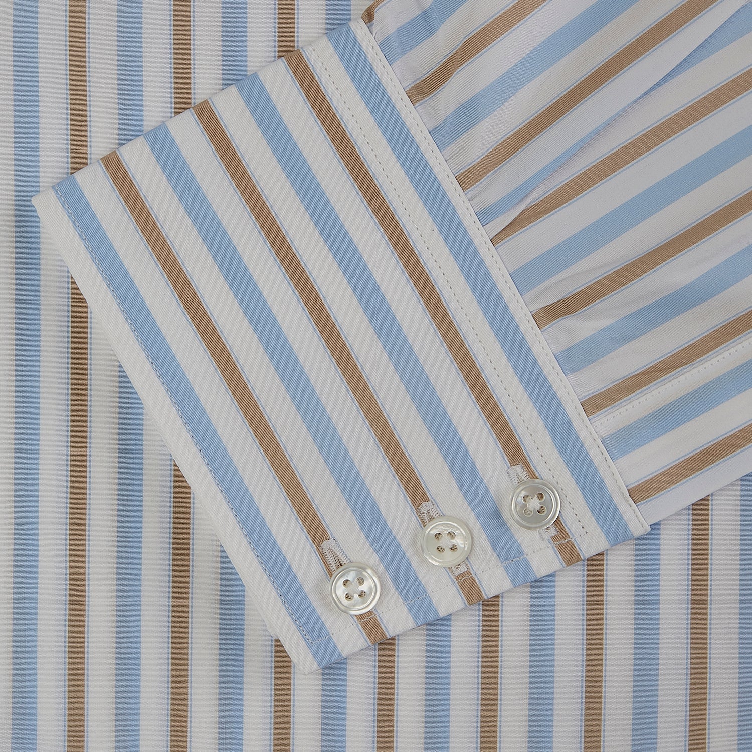 View 5 of product The Turnbull & Asser Blue and Brown Stripe Poplin Shirt features a T&A collar, three-button cuffs, and vertical blue, white, and tan stripes. This smart-casual shirt is displayed on a plain light background.