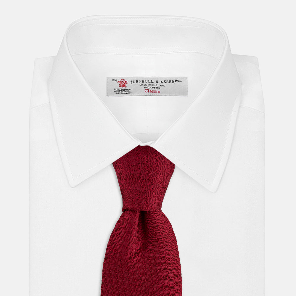 The Turnbull & Asser Burgundy Abstract Tonal Silk Jacquard Tie is shown rolled up with a subtle textured pattern on a plain white background—an elegant formalwear choice.