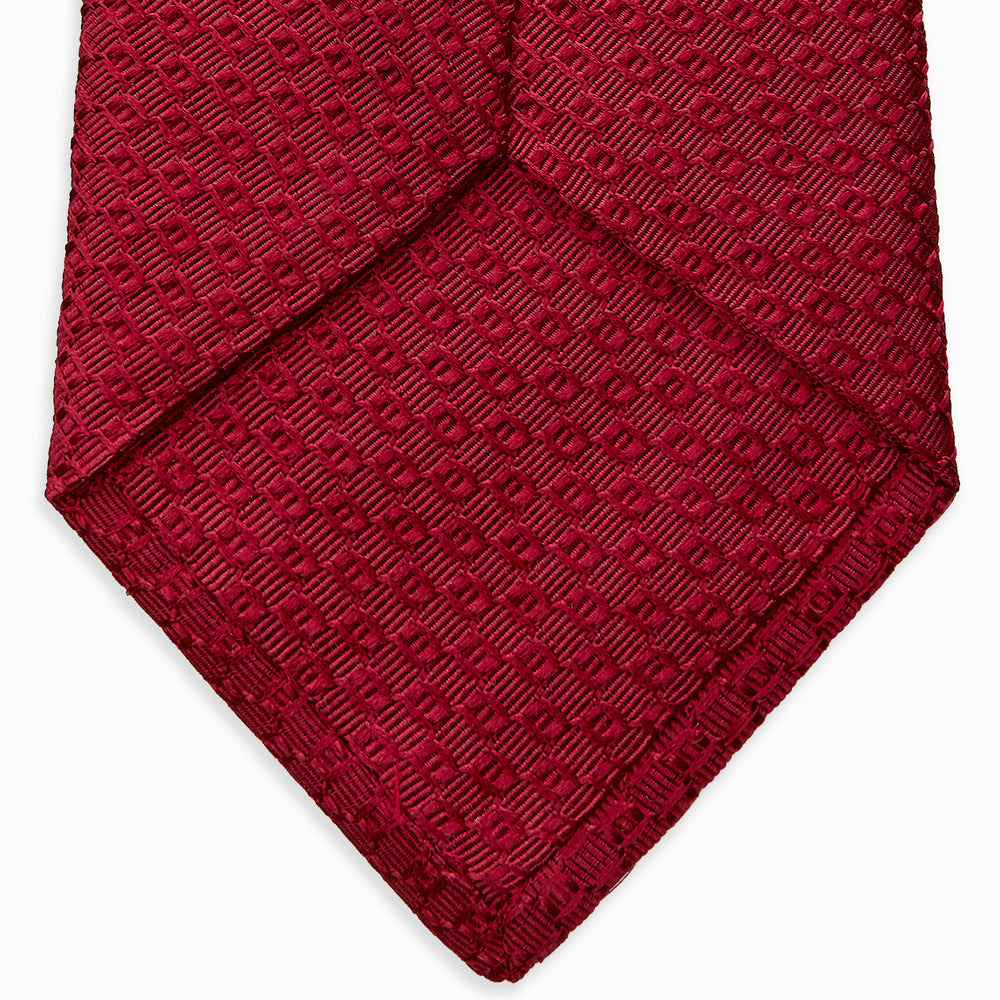 The Turnbull & Asser Burgundy Abstract Tonal Silk Jacquard Tie is shown rolled up with a subtle textured pattern on a plain white background—an elegant formalwear choice.