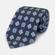 The Turnbull & Asser Blue Geometric Jacquard Tie is a rolled-up silk tie showcasing a repeating light blue and white geometric floral pattern with dotted accents, set against a plain light background.
