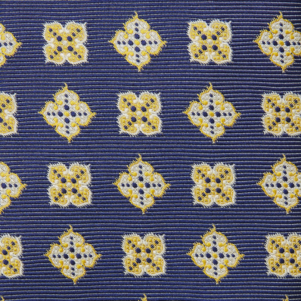 The Turnbull & Asser Yellow Geometric Jacquard Tie in navy features a repeating pattern of yellow geometric shapes with blue accents, presented rolled up on a white background.