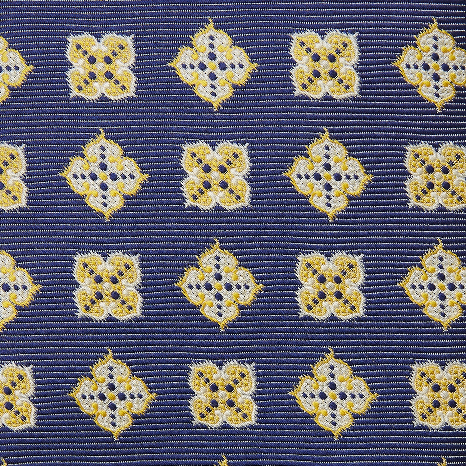 View 3 of product The Turnbull & Asser Yellow Geometric Jacquard Tie in navy features a repeating pattern of yellow geometric shapes with blue accents, presented rolled up on a white background.