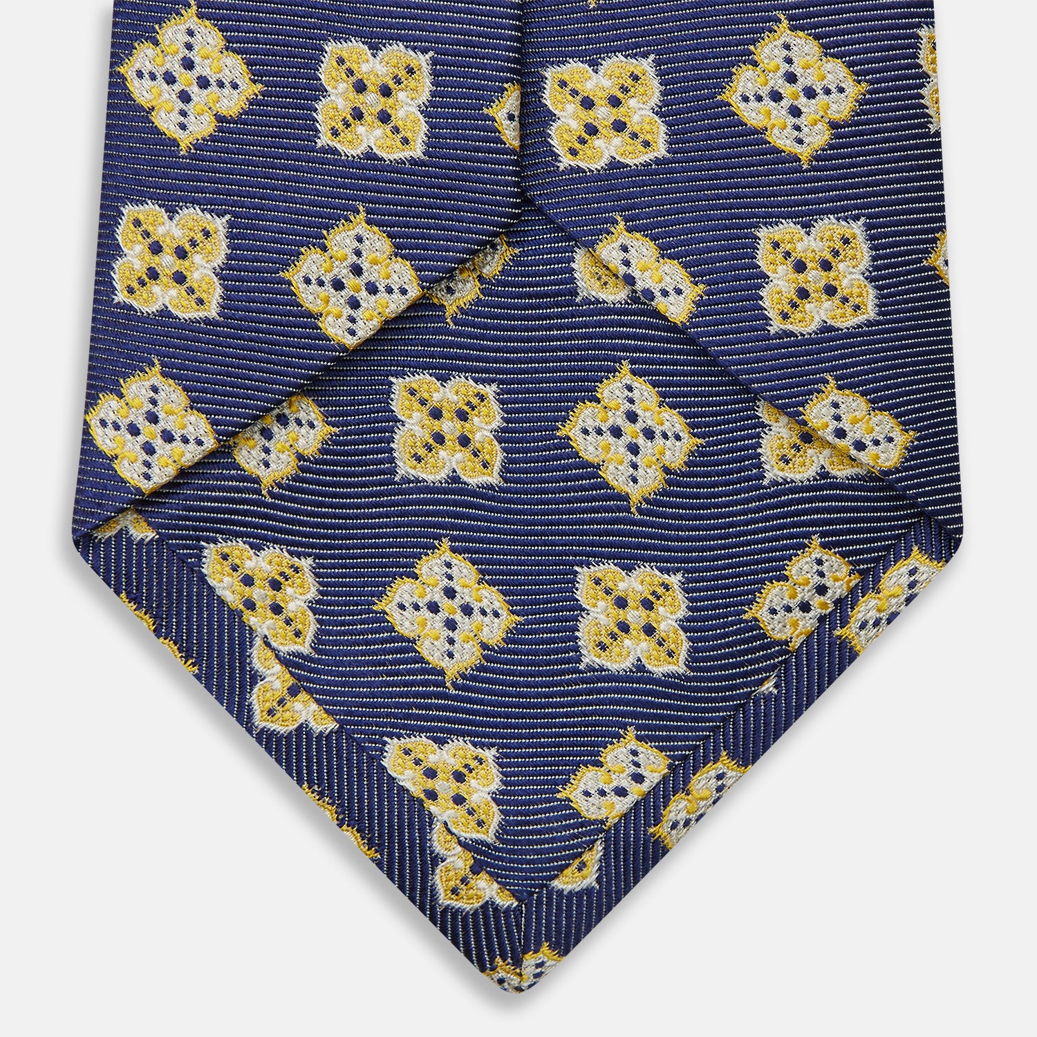 View 4 of product The Turnbull & Asser Yellow Geometric Jacquard Tie in navy features a repeating pattern of yellow geometric shapes with blue accents, presented rolled up on a white background.