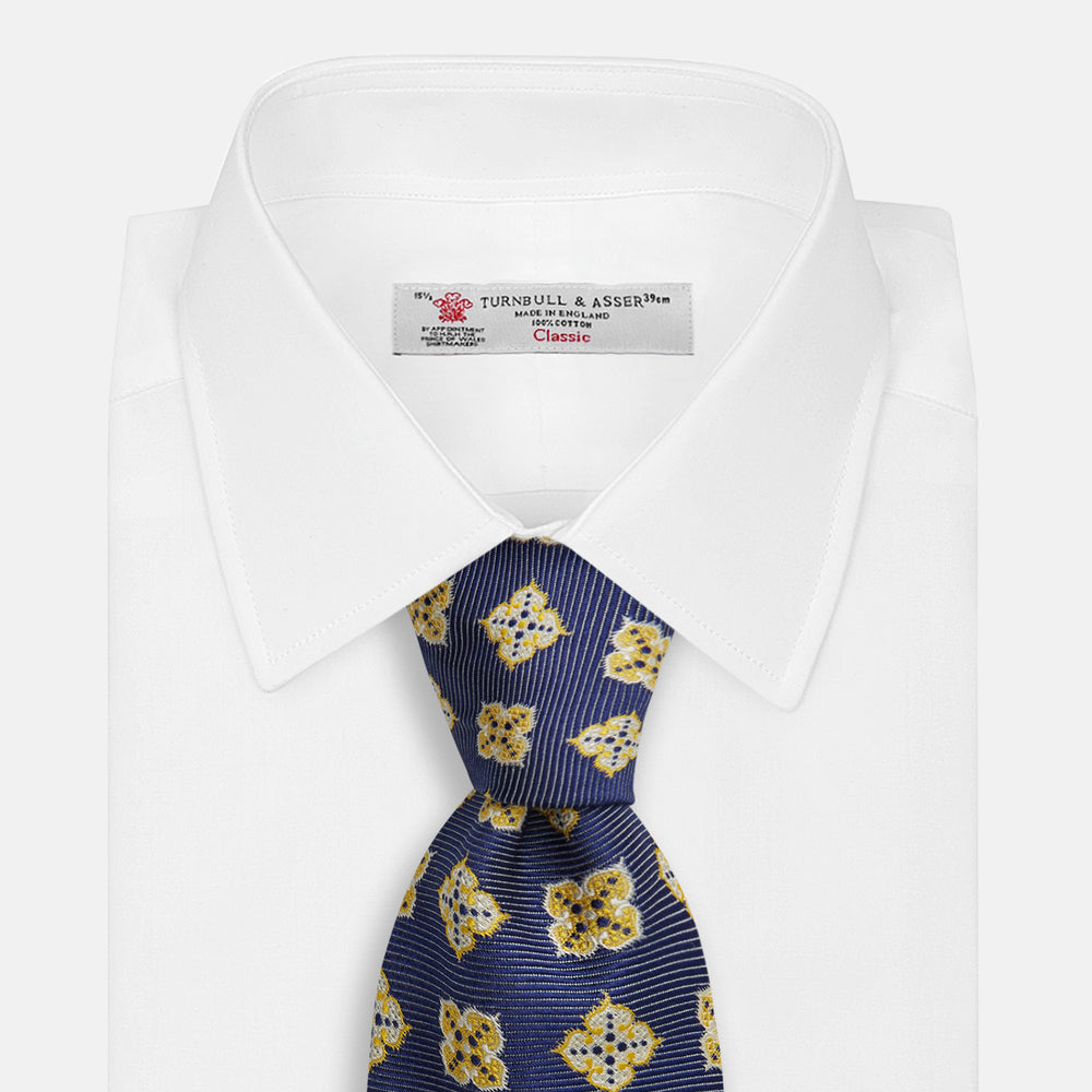 The Turnbull & Asser Yellow Geometric Jacquard Tie in navy features a repeating pattern of yellow geometric shapes with blue accents, presented rolled up on a white background.