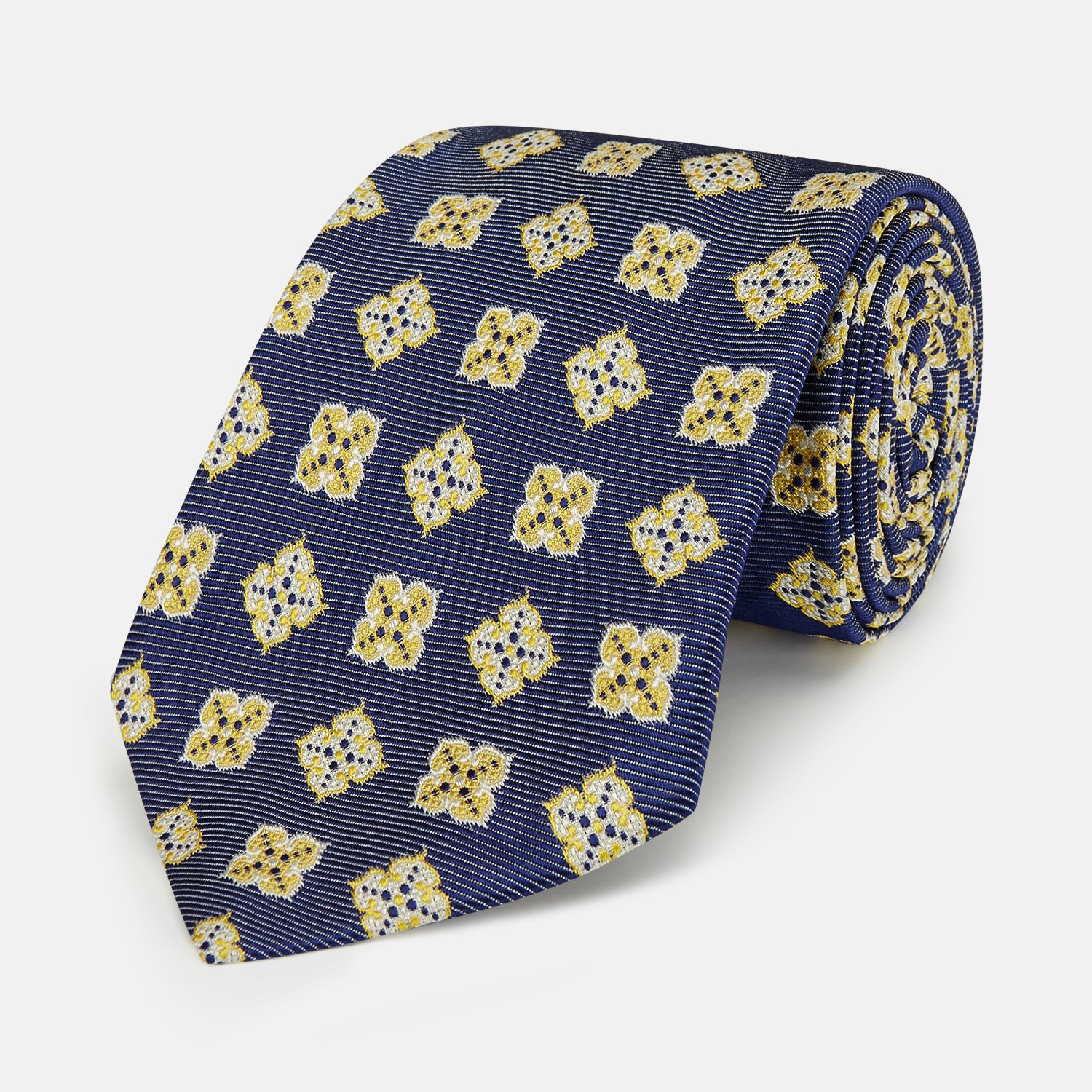 View 1 of product The Turnbull & Asser Yellow Geometric Jacquard Tie in navy features a repeating pattern of yellow geometric shapes with blue accents, presented rolled up on a white background.