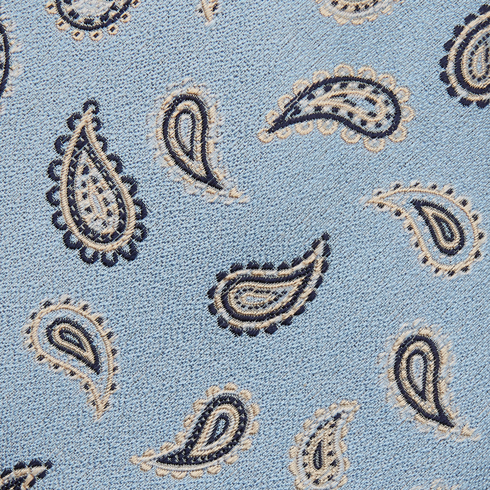 The Turnbull & Asser Sky Blue Renoir Paisley Tie, crafted in silk with a repeating navy and beige pattern, is shown rolled up with its pointed end forward on a plain white background.