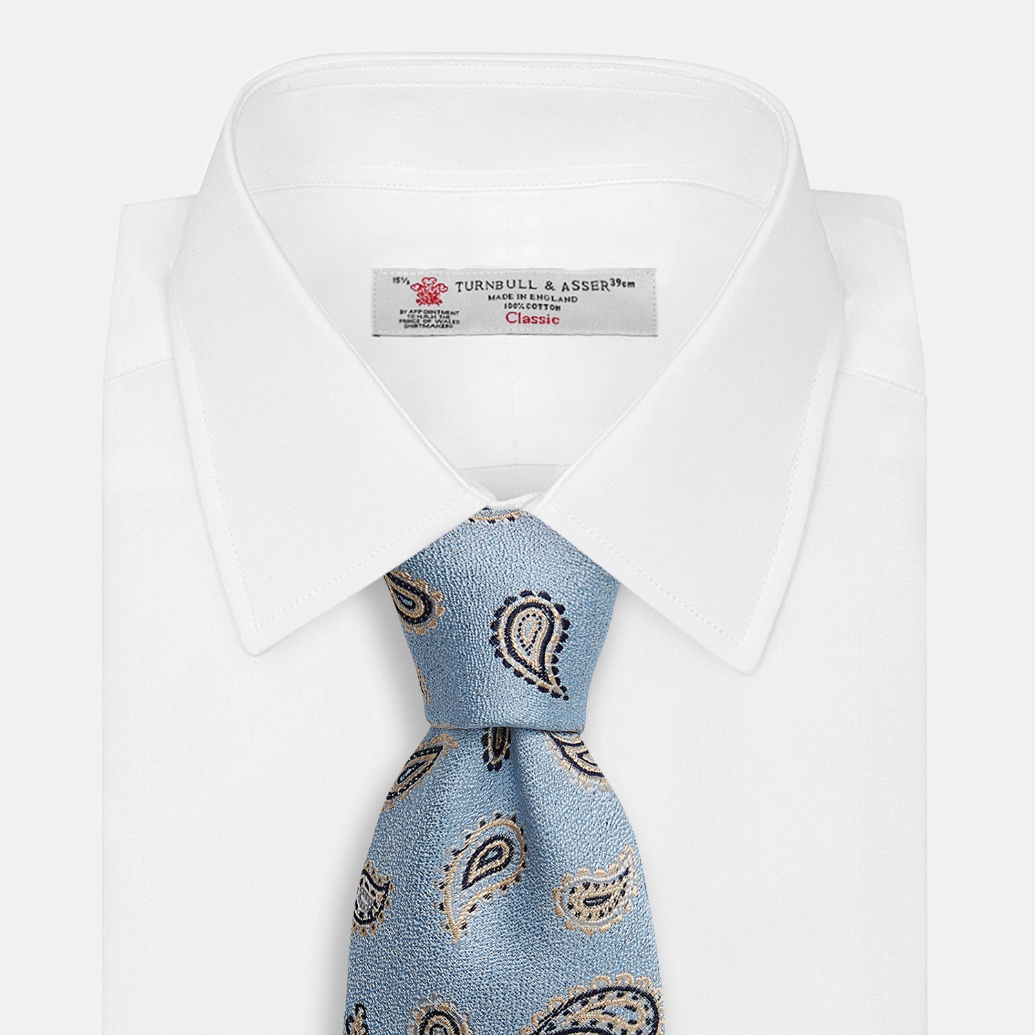 View 2 of product The Turnbull & Asser Sky Blue Renoir Paisley Tie, crafted in silk with a repeating navy and beige pattern, is shown rolled up with its pointed end forward on a plain white background.