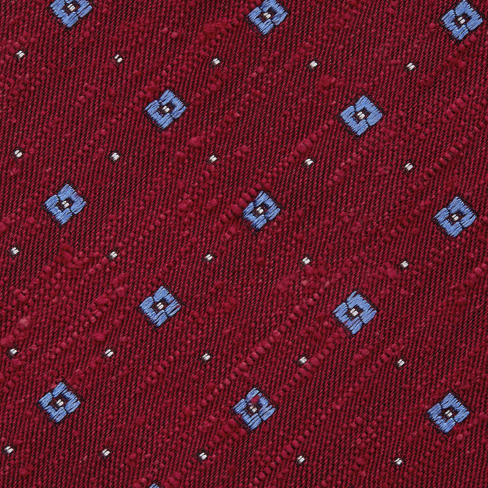 The Turnbull & Asser Red Square Silk Tie features a red and blue pattern with small white squares, elegantly rolled and displayed on a plain white background—a refined choice for men's accessories.
