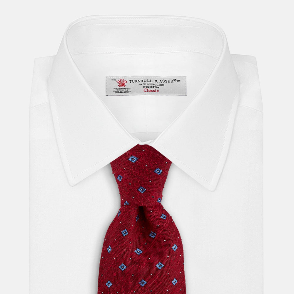 The Turnbull & Asser Red Square Silk Tie features a red and blue pattern with small white squares, elegantly rolled and displayed on a plain white background—a refined choice for men's accessories.