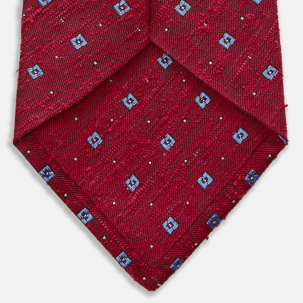 The Turnbull & Asser Red Square Silk Tie features a red and blue pattern with small white squares, elegantly rolled and displayed on a plain white background—a refined choice for men's accessories.