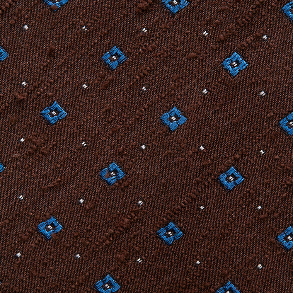 The Turnbull & Asser Brown Square Silk Tie, featuring a jacquard pattern of small blue squares and dots, is shown rolled up on a plain white background.