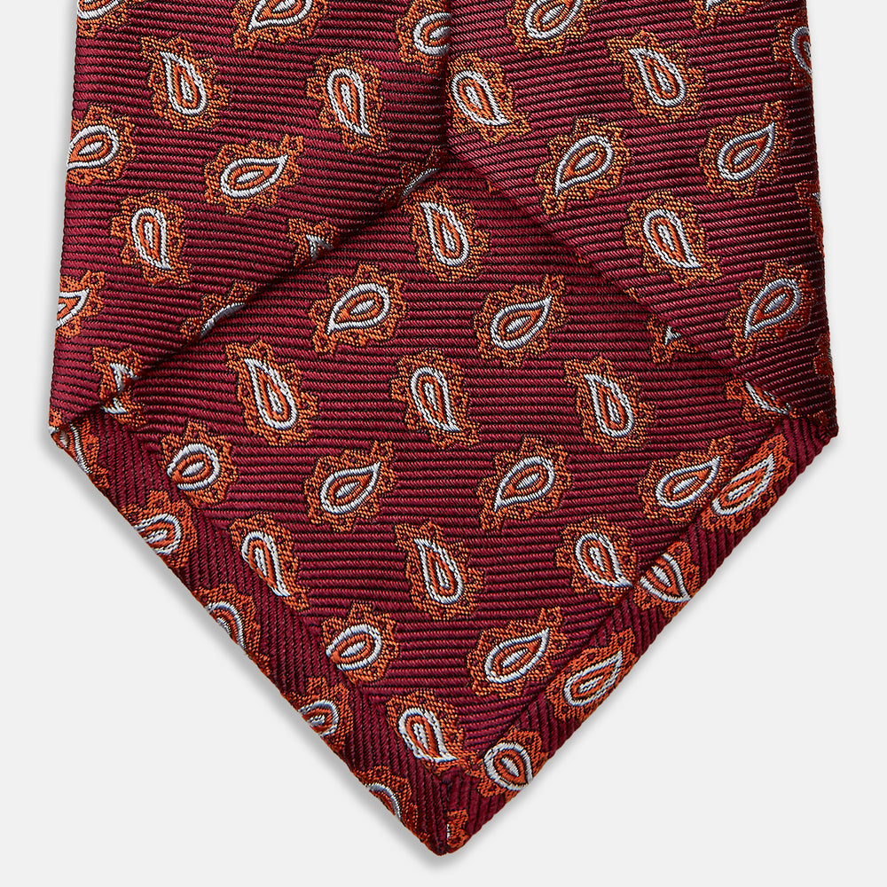 The Turnbull & Asser Red Abstract Paisley Silk Tie features bold orange and white paisley patterns on rich red silk—a stylish choice for fans of classic tailoring.