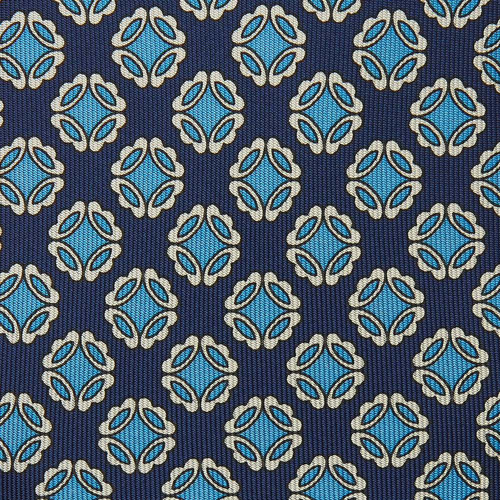 A rolled Navy Floral Geometric Tie by Turnbull & Asser, shown on a light background with light blue and white geometric floral motifs—a refined, stylish accessory.