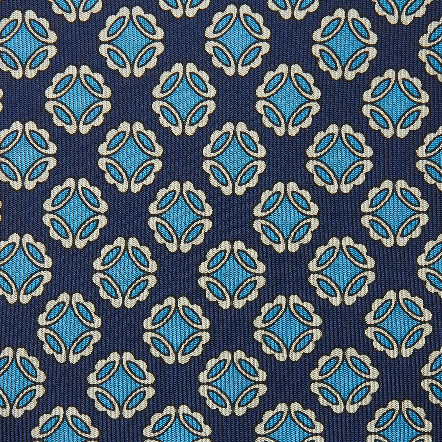 View 3 of product A rolled Navy Floral Geometric Tie by Turnbull & Asser, shown on a light background with light blue and white geometric floral motifs—a refined, stylish accessory.
