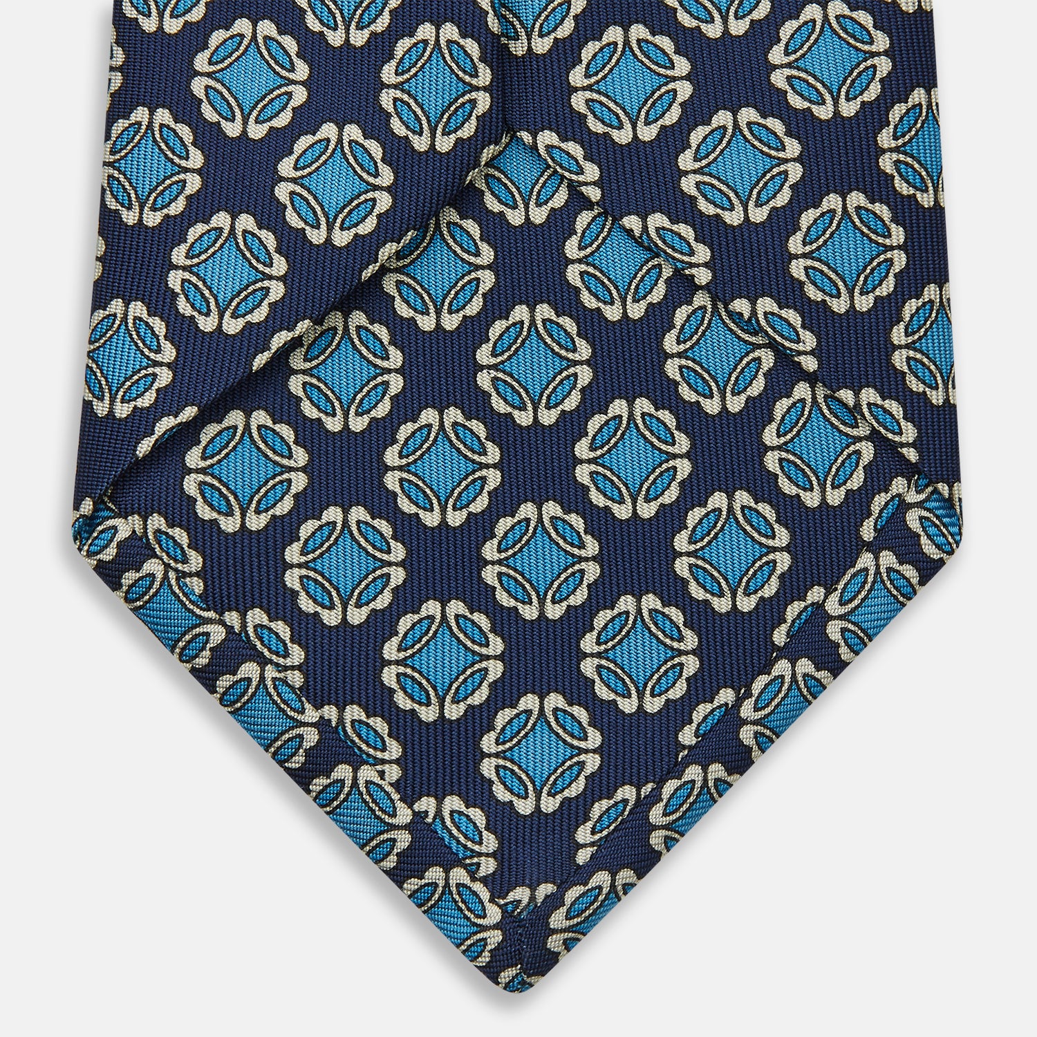 View 4 of product A rolled Navy Floral Geometric Tie by Turnbull & Asser, shown on a light background with light blue and white geometric floral motifs—a refined, stylish accessory.