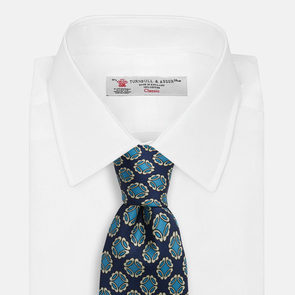 A rolled Navy Floral Geometric Tie by Turnbull & Asser, shown on a light background with light blue and white geometric floral motifs—a refined, stylish accessory.