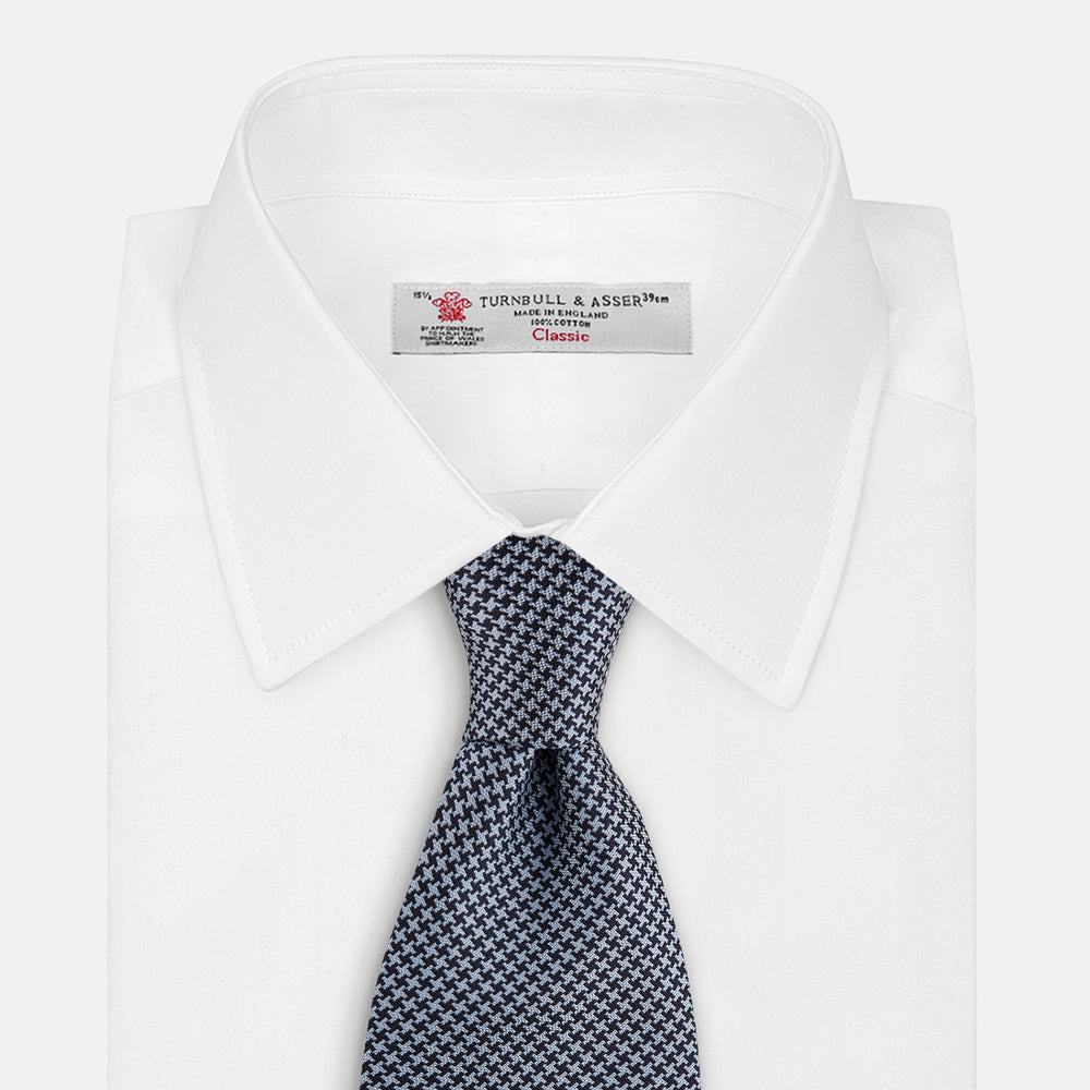 The Turnbull & Asser Blue Houndstooth Silk Tie, shown rolled on a plain white background, adds a refined touch to any sophisticated wardrobe.