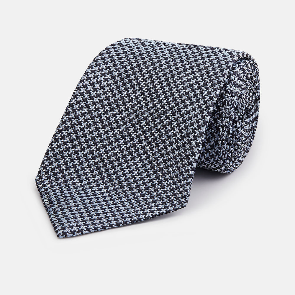 The Turnbull & Asser Blue Houndstooth Silk Tie, shown rolled on a plain white background, adds a refined touch to any sophisticated wardrobe.