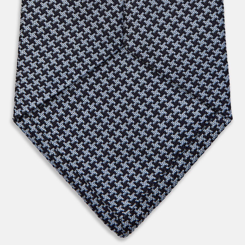 The Turnbull & Asser Blue Houndstooth Silk Tie, shown rolled on a plain white background, adds a refined touch to any sophisticated wardrobe.