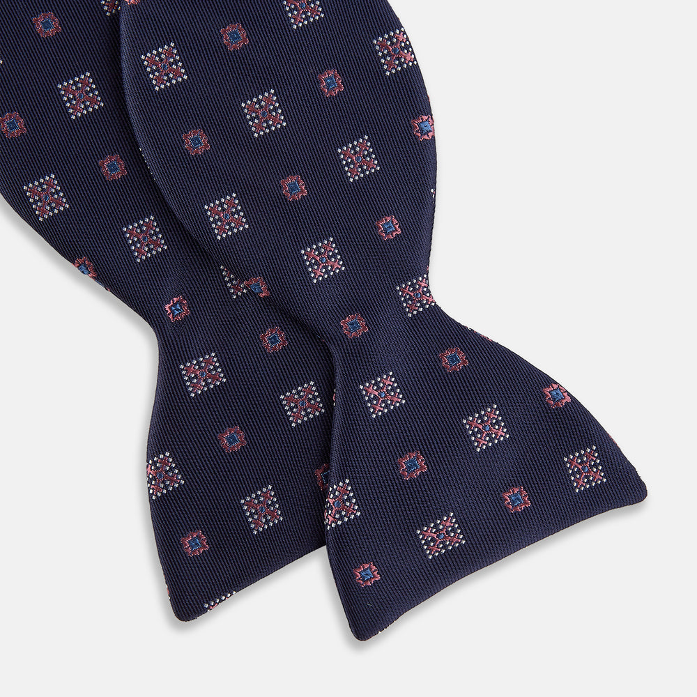 The Turnbull & Asser Pink Shields Bow Tie features a pink pattern with shield motifs, ideal for formal occasions and displayed on a plain white background.