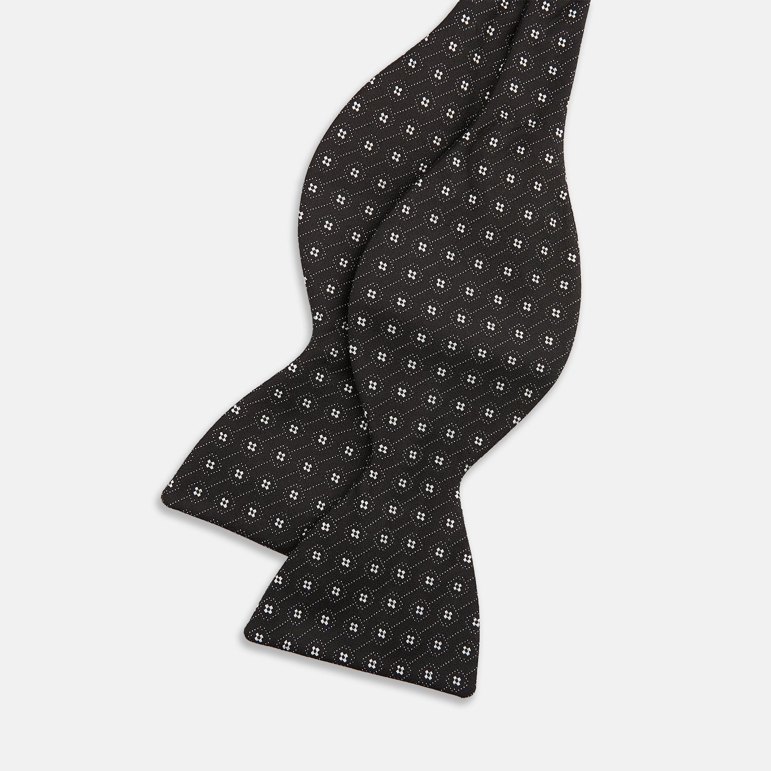 View 2 of product The Floral Piqué Monochrome Silk Bow Tie by Turnbull & Asser, featuring a repeating pattern of small white dots and hexagons on black silk, is ideal for formalwear or a dinner suit and is shown against a plain white background.