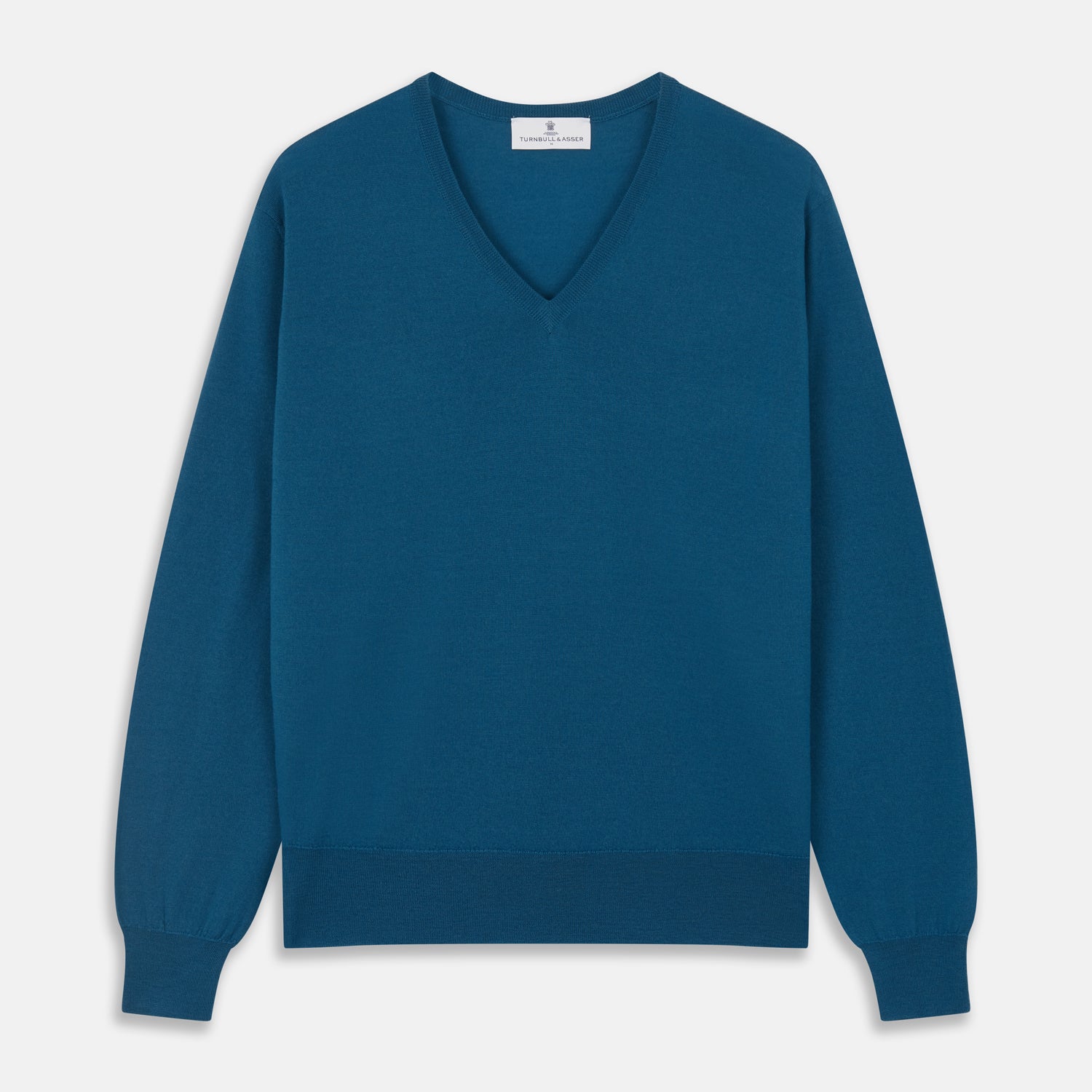 View 1 of product The Turnbull & Asser Ocean Blue Merino Kennedy V-Neck Jumper, shown flat on a white background, features ribbed cuffs and hem with a visible branded label at the neckline.