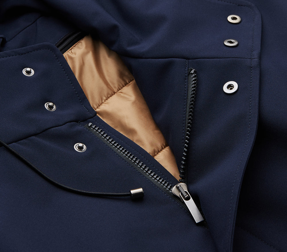The Turnbull & Asser Navy Walter Sealup Parka with Detachable Liner features silver snap buttons, front flap pockets, and a drawstring hem. Styled against a white background, this waterproof parka offers both elegance and practicality for wet weather.