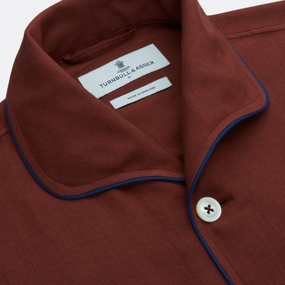The Turnbull & Asser Red Cotton-Cashmere Pyjama Set features a rust-red long-sleeve button-up top with chest pocket and matching waist-tied pants, shown on a plain white background.
