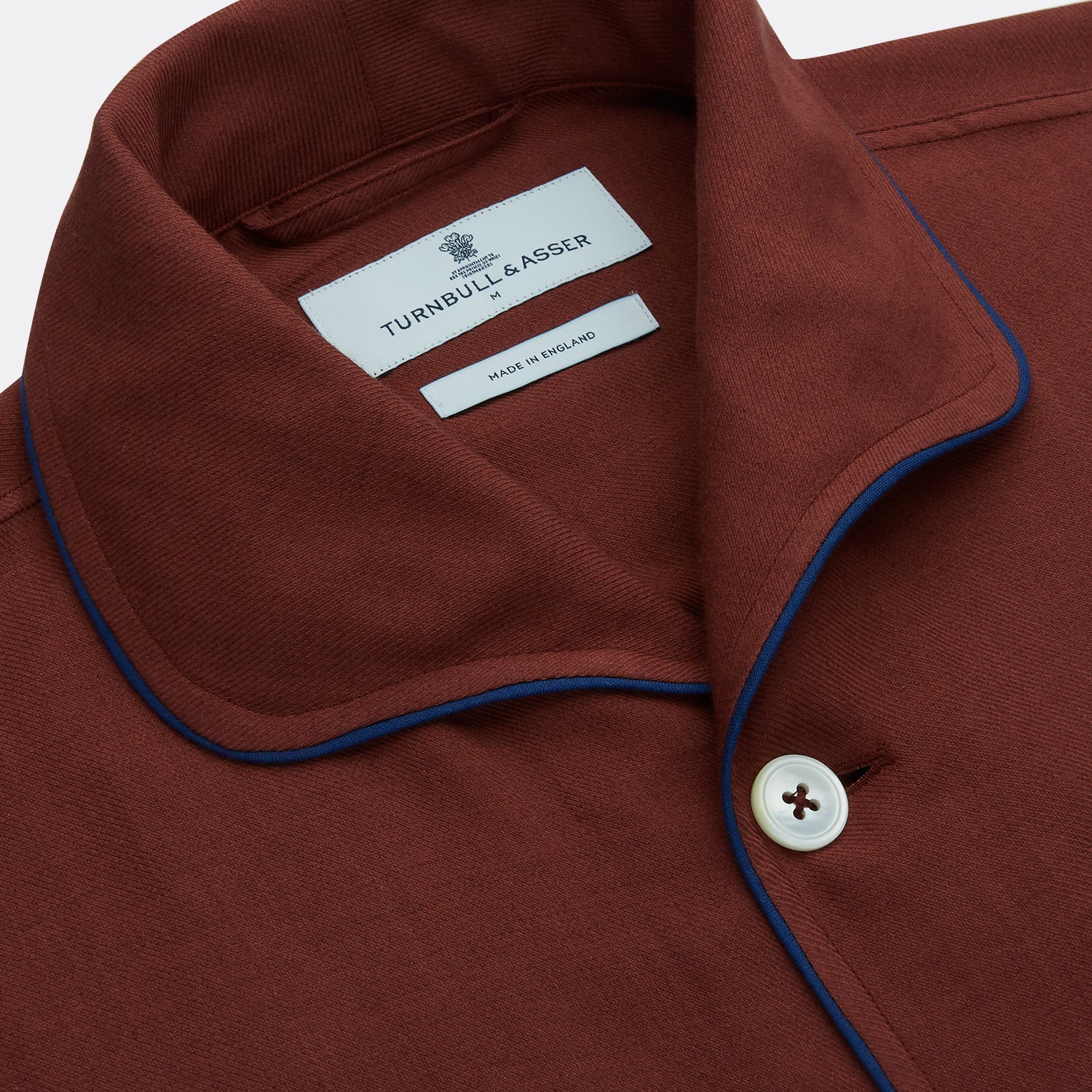 View 3 of product The Turnbull & Asser Red Cotton-Cashmere Pyjama Set features a rust-red long-sleeve button-up top with chest pocket and matching waist-tied pants, shown on a plain white background.