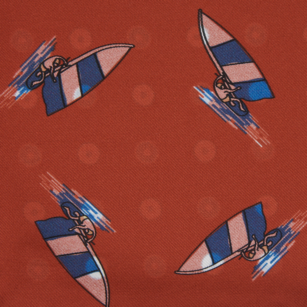 The Turnbull & Asser Red Windsurfer Double-Faced Silk Print Pocket Square features a vibrant windsurfer pattern on silk with a dark blue border and the brand subtly printed in one corner.