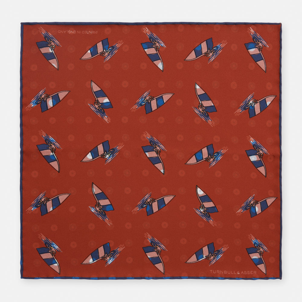 The Turnbull & Asser Red Windsurfer Double-Faced Silk Print Pocket Square features a vibrant windsurfer pattern on silk with a dark blue border and the brand subtly printed in one corner.