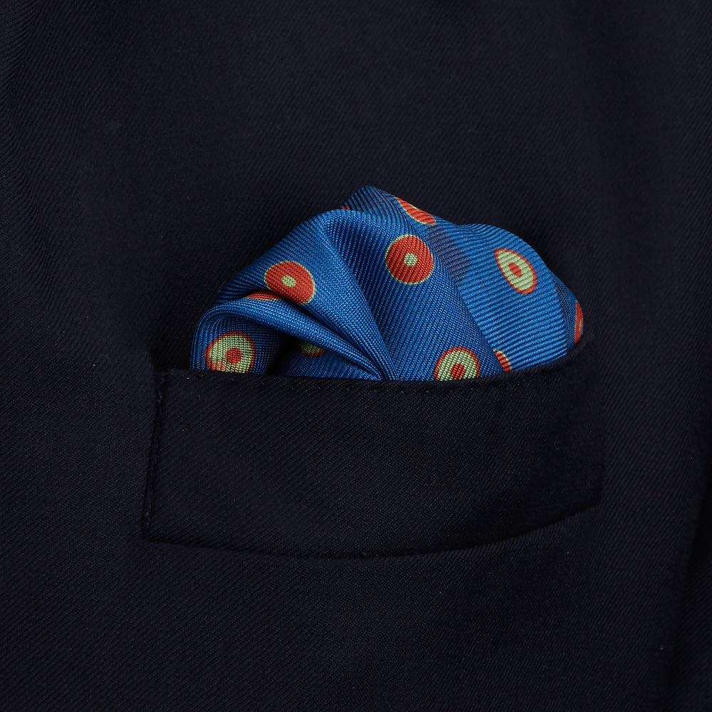 The Turnbull & Asser Blue Windsurfer Double-Faced Silk Print Pocket Square features a blue silk design with colorful windsurfers and vivid red edges, finished with the Turnbull & Asser logo in one corner.