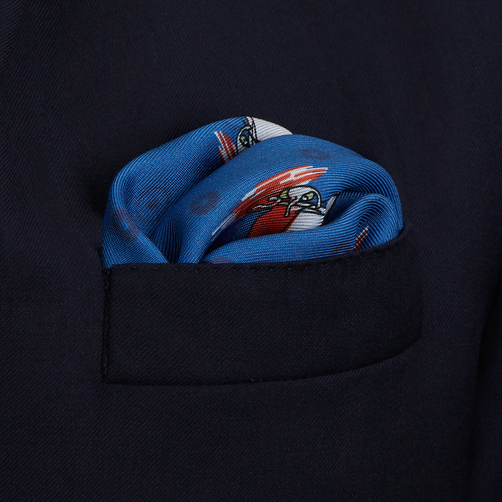 The Turnbull & Asser Blue Windsurfer Double-Faced Silk Print Pocket Square features a blue silk design with colorful windsurfers and vivid red edges, finished with the Turnbull & Asser logo in one corner.
