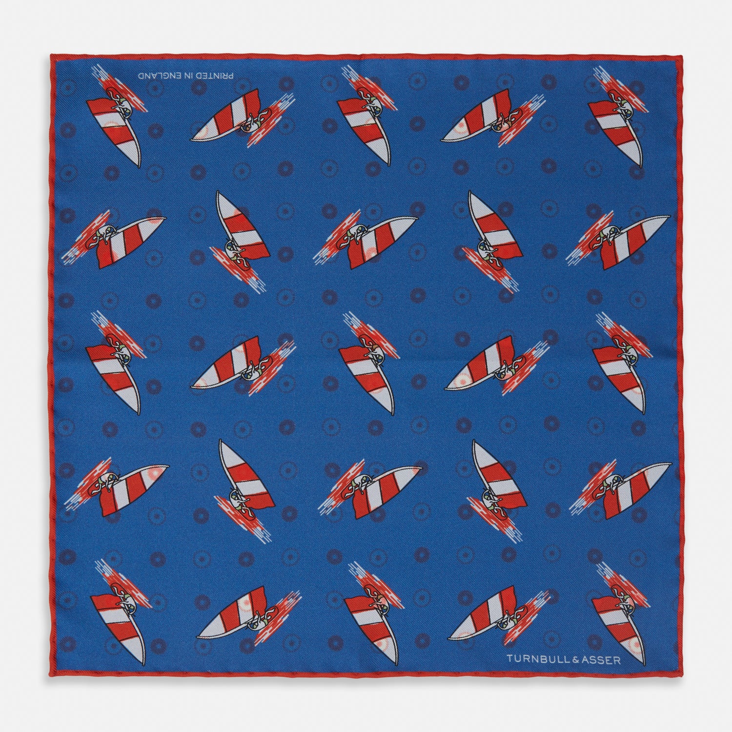 View 1 of product The Turnbull & Asser Blue Windsurfer Double-Faced Silk Print Pocket Square features a blue silk design with colorful windsurfers and vivid red edges, finished with the Turnbull & Asser logo in one corner.