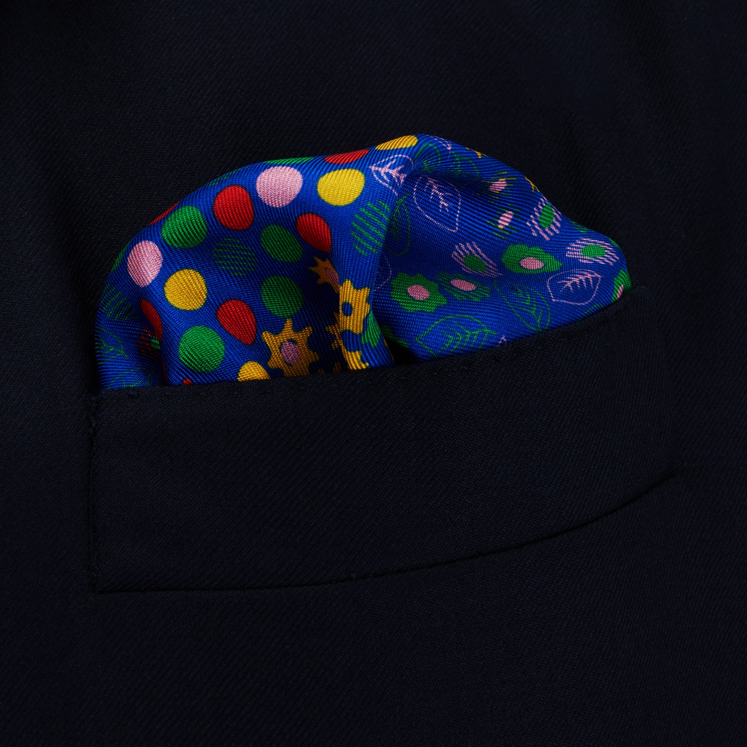 View 2 of product The Turnbull & Asser Navy Abstract Floral Silk Pocket Square features a vibrant blue base with colorful flowers, dots, and leaves arranged in a symmetrical geometric design for a sharp, tailored look.