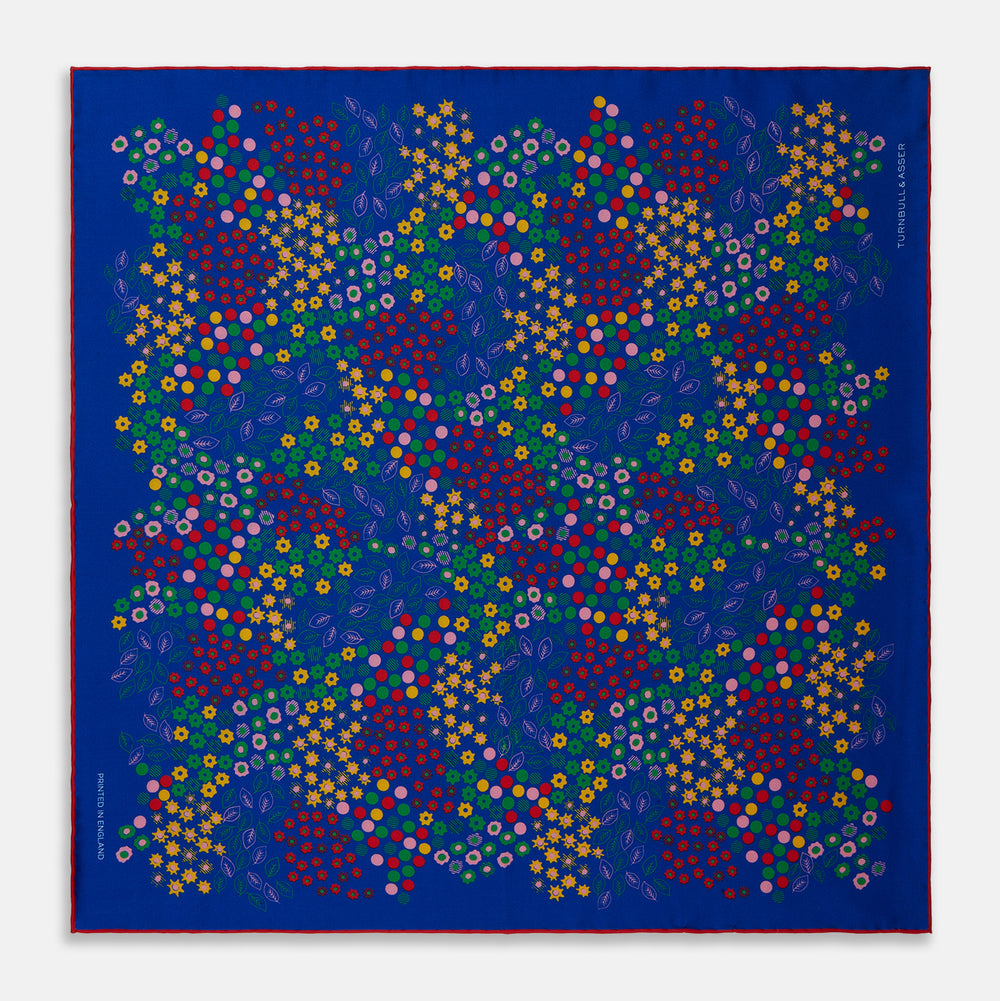 The Turnbull & Asser Navy Abstract Floral Silk Pocket Square features a vibrant blue base with colorful flowers, dots, and leaves arranged in a symmetrical geometric design for a sharp, tailored look.