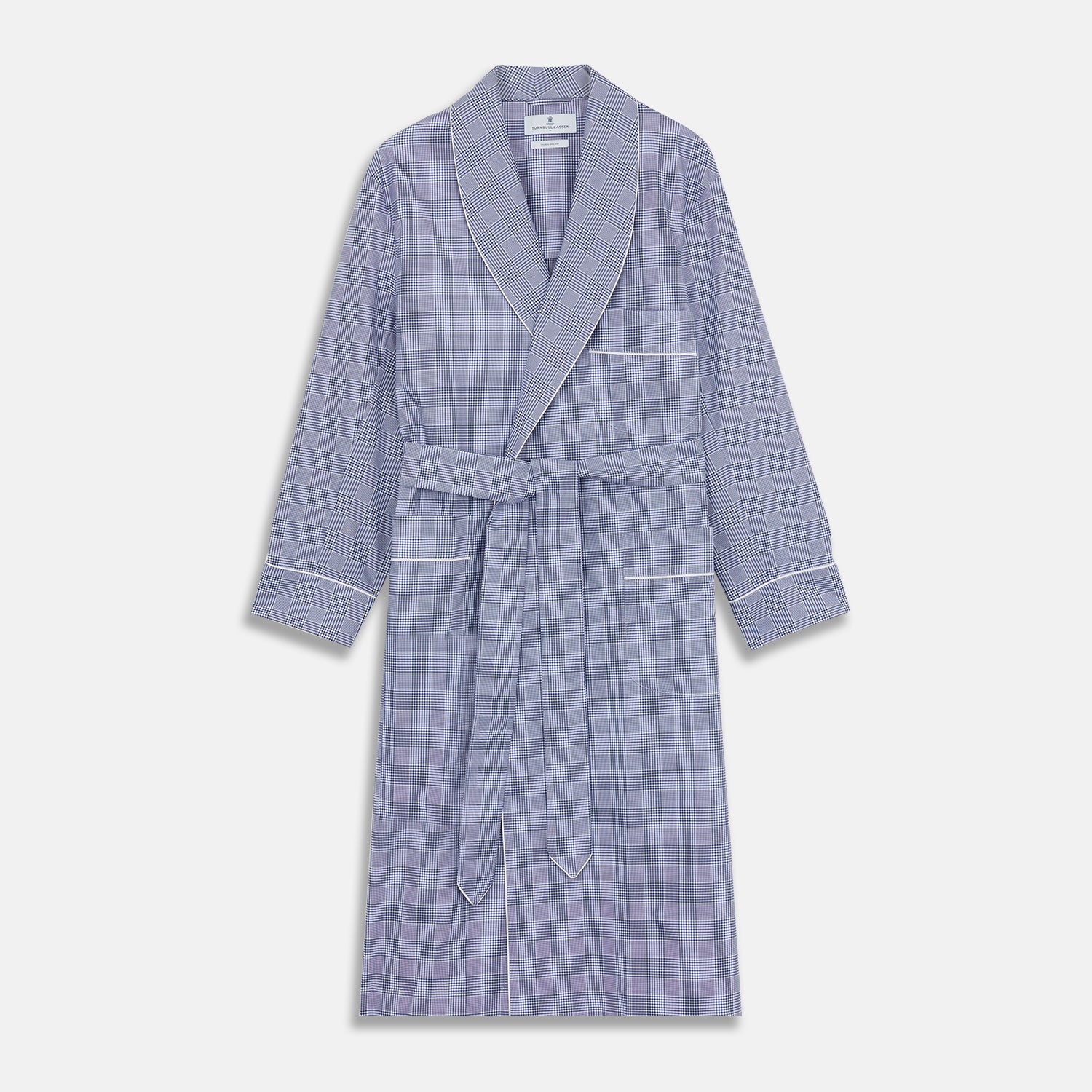 View 1 of product The Turnbull & Asser Navy Check Cotton Gown features long sleeves, white piping, a shawl collar, chest pocket, and matching waist belt, all in a blue plaid pattern. Shown against a plain white background.