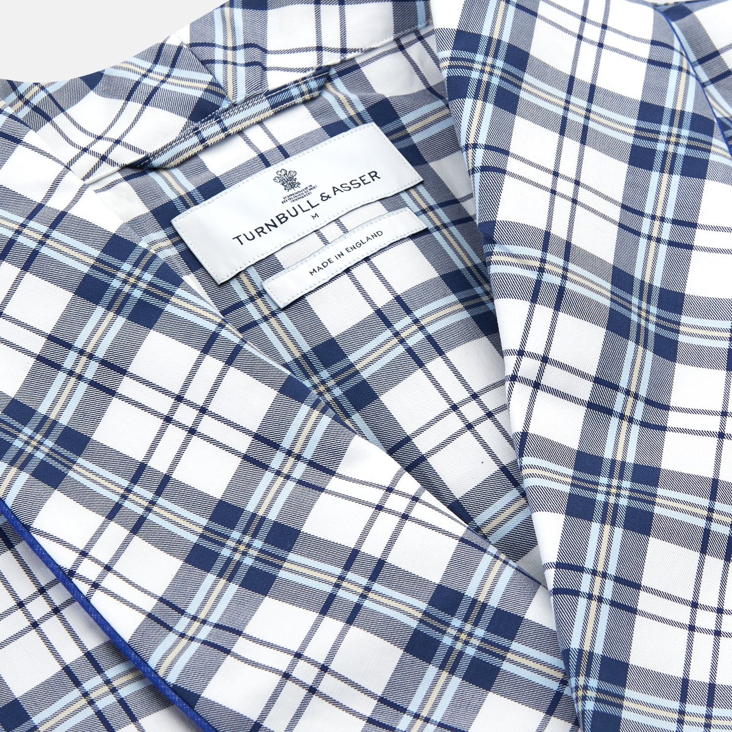 View 2 of product The Turnbull & Asser Blue Check Cotton Gown features long sleeves, a knee-length cut, shawl collar, and matching waist belt in a blue check pattern, shown against a plain white background.