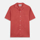 The Turnbull & Asser Crimson Delave Linen Holiday Fit Shirt features a solid brick-red hue, short sleeves, single chest pocket, and revere collar—perfect resort wear—shown laid flat on white.