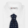 View 2 of product The Turnbull & Asser Navy Floral Emblem Tie displays a repeating pattern of small light blue, white, and yellow floral and diamond motifs, highlighting refined elegance, shown rolled up on a white background.