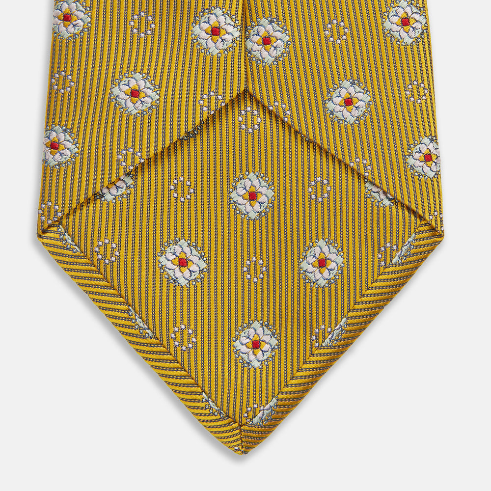 The Yellow Multi Floral Motif Silk Tie by Turnbull & Asser features subtle diagonal stripes and small white, blue, and orange floral motifs—a perfect summer palette, shown rolled up on a plain white background.
